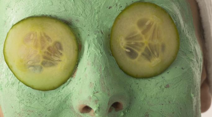 Young Woman Wearing Facial Cream and Cucumber Slices Over Eyes